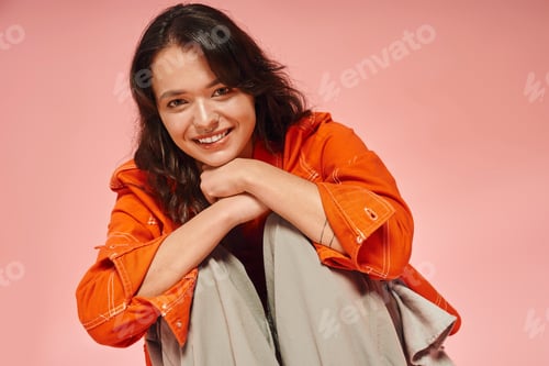 Preview: Stylish young woman poses in trendy attire against a vibrant pink backdrop during a photoshoot
