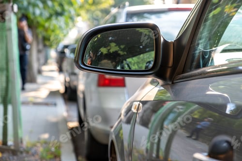 Preview: Close up of rearview mirror of a car parked near curb on the side of the street on a parking lot.