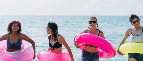 Preview: Teenagers laughing and playing in the sea with colorful swim rings, enjoying youthful summer fun.
