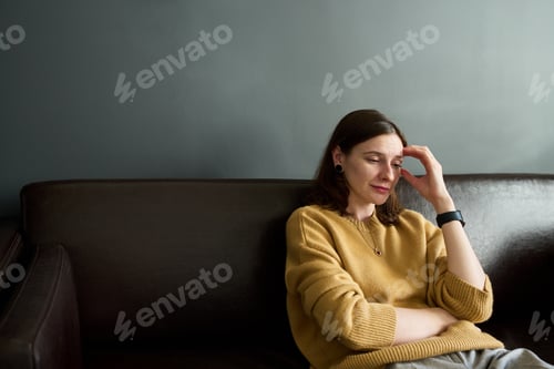 Preview: Young Adult Caucasian Woman Sitting on Sofa Looking Thoughtful and Reflecting