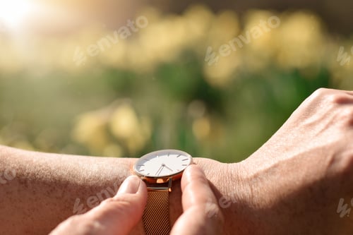 Preview: Woman is checking the time on her wristwatch with blurry yellow spring flowers in the background