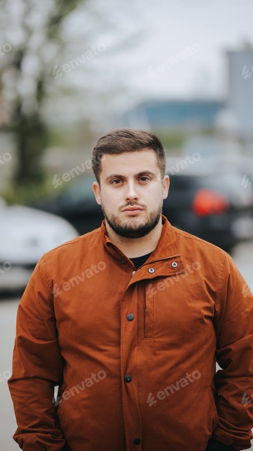 Preview: Vertical shot of a Caucasian man standing in the street, wearing a jacket during daylight