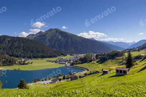 Preview: Mesmerizing green land with small houses and high hills against a cloudy sky on a sunny day
