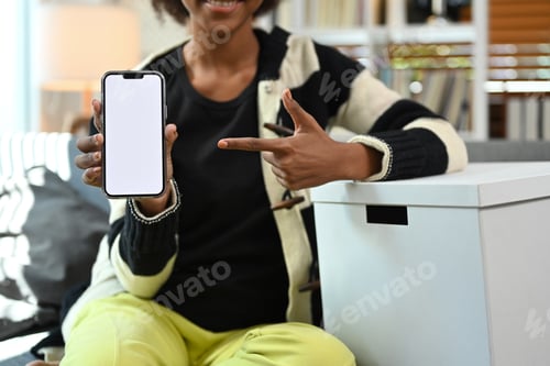 Preview: Cropped image of smiling woman pointing at smart phone and smiling at camera.