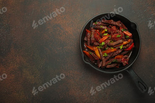 Preview: Lomo saltado, beef and red pepper stir fry cooking in cast iron pan, traditional Peruvian dish