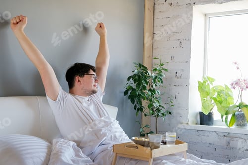 Preview: Young man waking up and having breakfast in bed