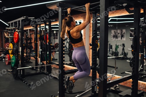 Preview: Determined sportswoman doing pull ups in modern fitness center, empowering strength training workout