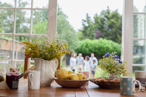 Preview: Kitchen table with breakfast foods, family in garden behind, focus on table