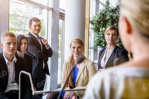 Preview: Businesswomen and men listening to speaker in office conference room
