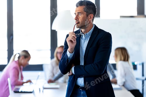 Preview: Handsome businessman looking to sideways while his colleagues are working on coworking place.
