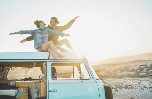 Preview: Happy couple sitting on top of minivan roof at sunset