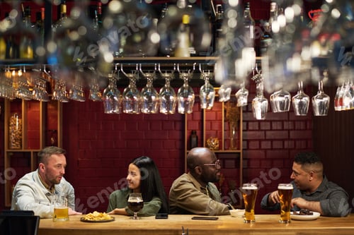 Preview: Row of young intercultural people sitting along bar counter and chatting