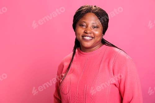 Preview: Portrait of african american model smiling at camera while posing happy in studio with pink