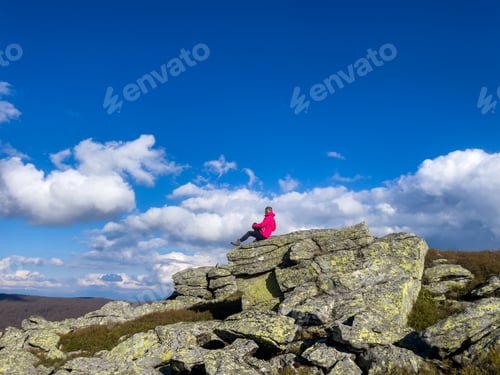 Preview: Woman hiker sitting on a cliff in the mountains