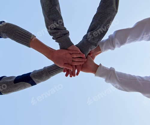 Preview: Low angle shot of three young friends putting their hands together against a blue sky