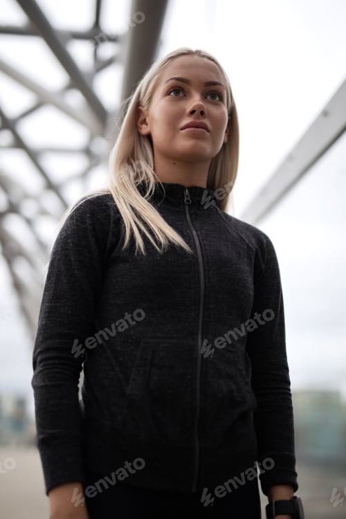 Preview: Urban scandinavian woman in workout outfit standing on a bridge