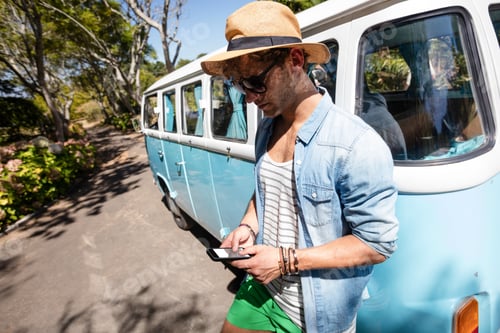Preview: Man standing near campervan and using mobile phone