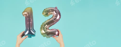 Preview: Hand is holding balloon number twelve on mint or tiffany blue background.