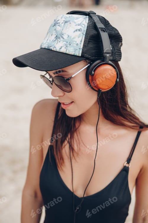 Preview: beautiful young woman in cap and sunglasses listening music with headphones