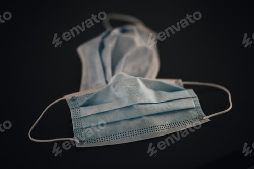 Preview: closeup of used personal protective equipment surgical medical masks sitting on a dark table