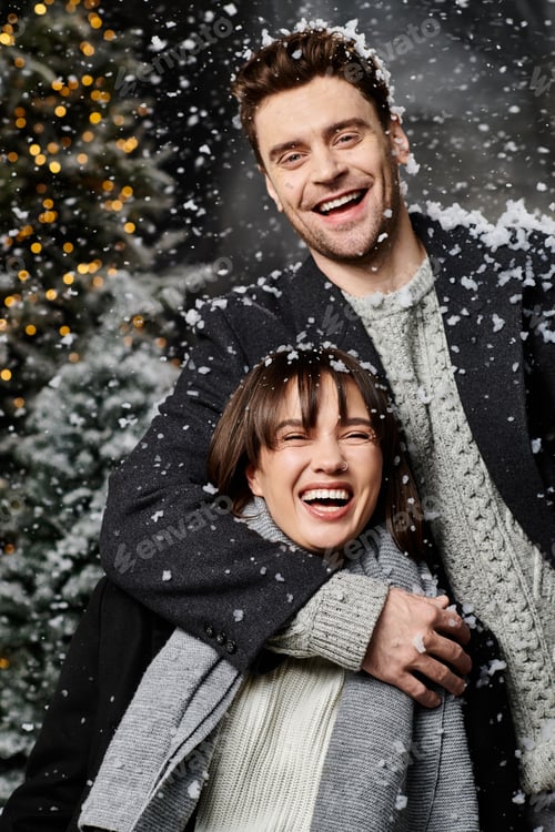 Preview: A joyful couple celebrating Christmas in warm winter coats among snowy pine trees