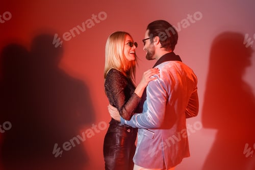 Preview: Cheerful woman in sunglasses hugging stylish boyfriend on red background
