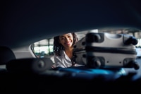 Preview: Smiling woman puts suitcases into the car, parking