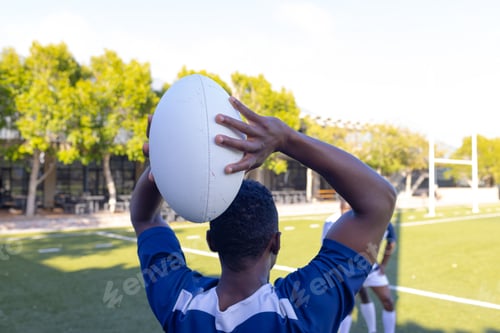 Preview: Group of three African American young male athletes training with a rugby ball on a field outdoors
