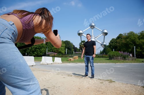 Preview: Young Hispanic girl taking a photo of her boyfriend posing at Atomium in Brussels, Belgium