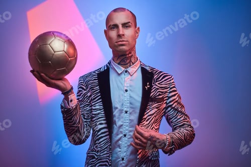 Preview: Elegant tattooed male model posing with a golden soccer ball in a studio