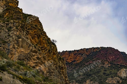 Preview: Landscape of rocks covered in greenery under a cloudy sky at daytime
