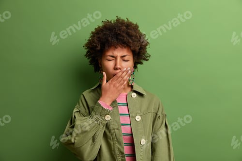 Preview: Sleepy exhausted African American woman covers mouth with palm, needs sleep, wakes up early in morni