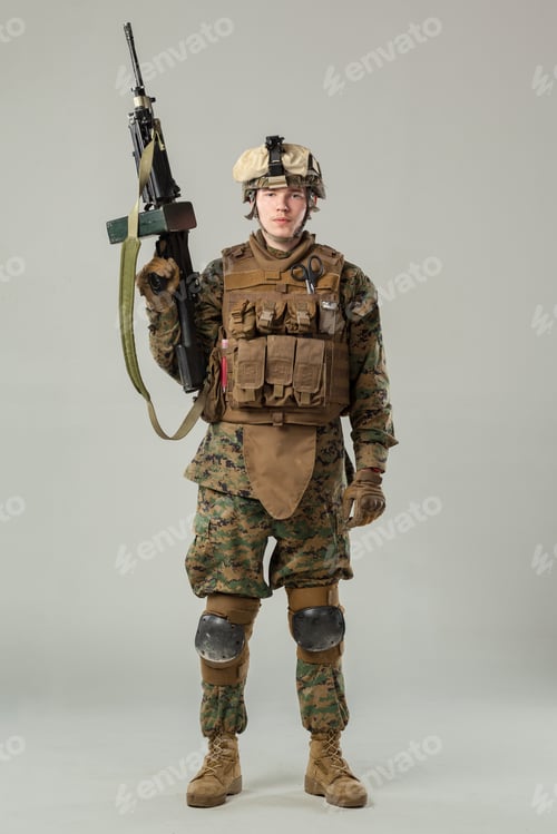 Preview: Soldier stands in military gear holding a rifle in a neutral setting indoors
