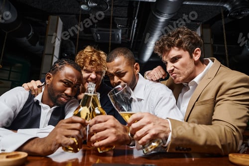 Preview: four multicultural colleagues in formal wear toasting with beer in bar, men spending time after work