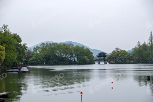 Preview: West Lake, Hangzhou, China. Traditional Pavilion bridge, spring trees, cloudy sky and calm water.