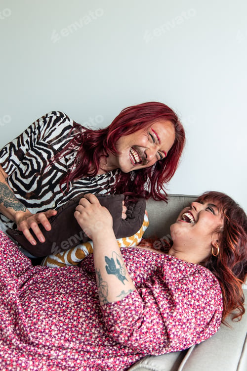 Preview: Non-binary friends laughing and having fun on sofa at home