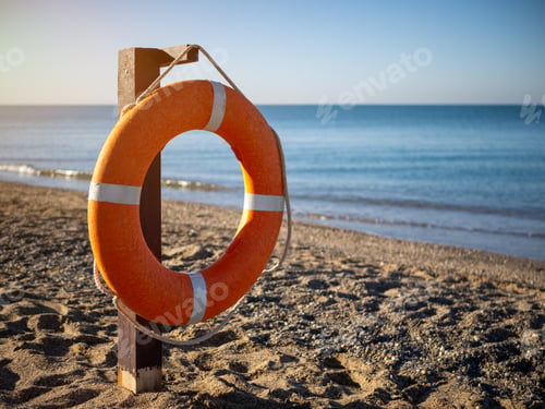 Preview: Bright orange lifebuoy on a sandy beach on a Sunny summer day.