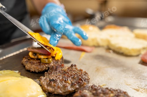 Preview: Cook adding cheese on a tasty burger with bacon and mushrooms