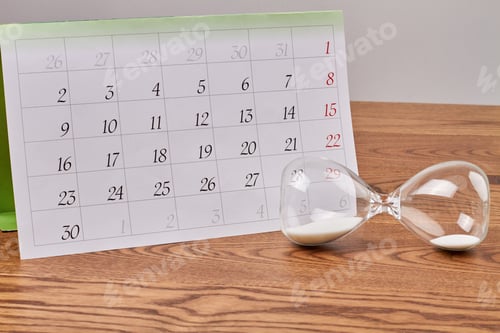 Preview: Hourglass with white sand and month calendar on wooden desk.