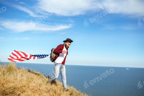 Preview: 4th of July. American Flag. Traveler with the flag of America. The man in a hat, a backpack