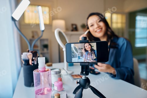 Preview: Close up of happy Asian influencer recording makeup vlog with mobile phone.