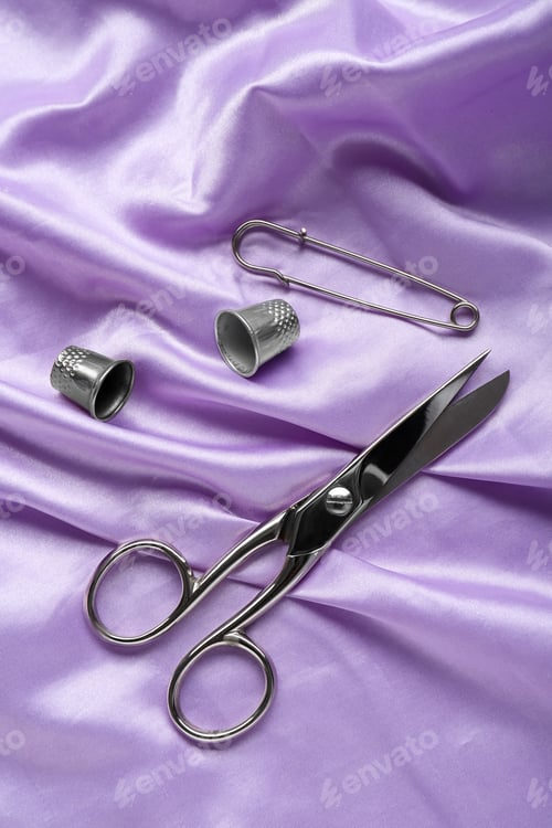 Preview: Silver thimbles and other sewing accessories on purple cloth, flat lay