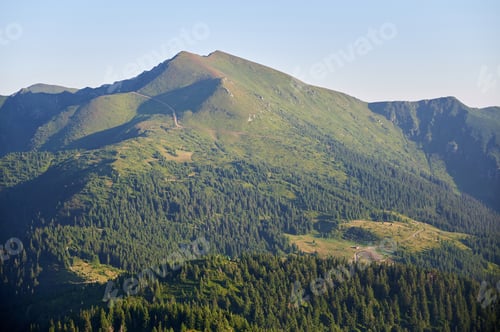 Preview: Expansive view of lush green mountain valleys under clear blue sky.