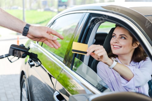 Preview: selective focus of happy woman sitting in car and giving credit card to worker at gas station