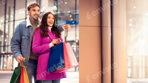 Preview: Happy young couple pointing standing with shopping bags outside mall