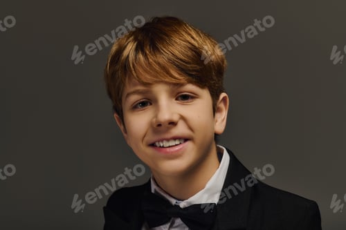 Preview: Elegant preteen boy in a stylish tuxedo with a bow tie posing in a studio setting