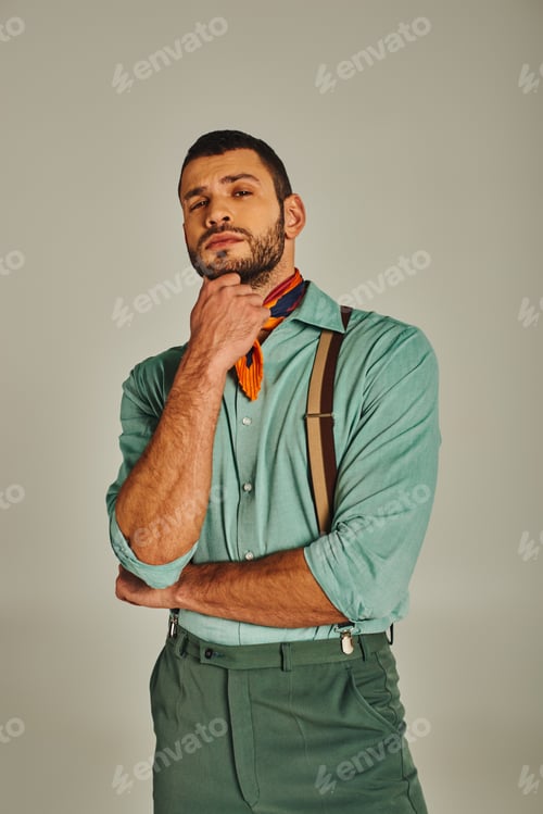 Preview: thoughtful man in suspenders and bright neckerchief looking at camera on grey, vintage fashion