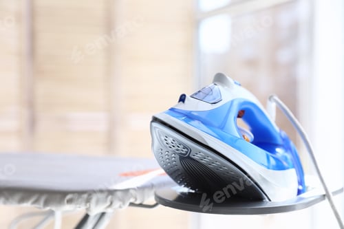 Preview: Modern electric iron on board indoors, space for text. Household appliance
