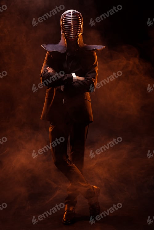 Preview: Full length view of kendo fighter in formal wear and helmet standing with crossed arms on dark