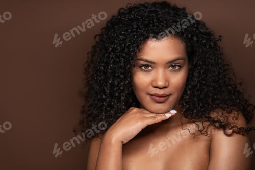 Preview: Woman with curly hair poses elegantly against a brown background
